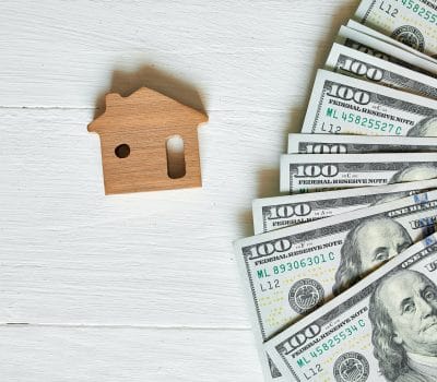 we buy houses for cash - Small wooden house and hundred dollar on white background