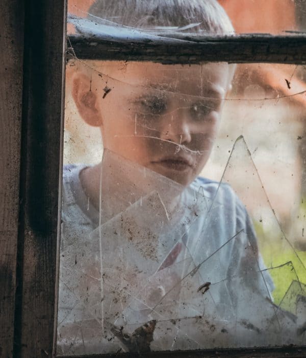 Boy looking through a broken window